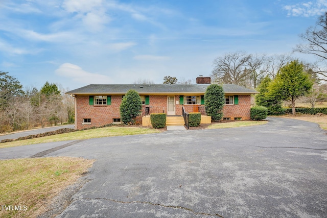 single story home with a front yard, brick siding, covered porch, and a chimney