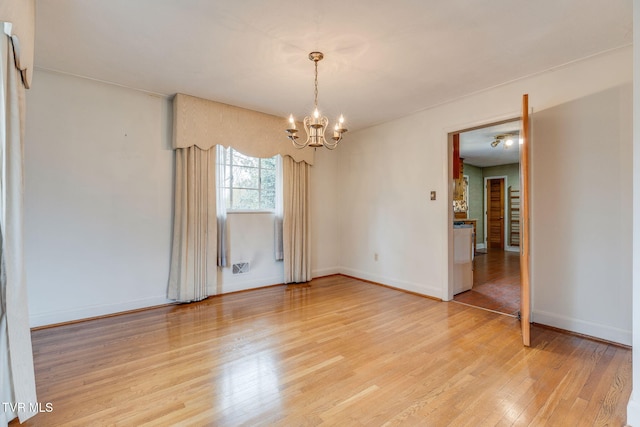 spare room featuring an inviting chandelier, baseboards, and light wood-style floors