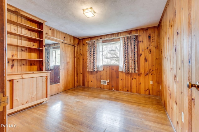 spare room with a textured ceiling, light wood-style flooring, and wooden walls