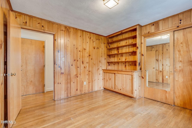 unfurnished room with built in features, wood walls, light wood finished floors, and a textured ceiling