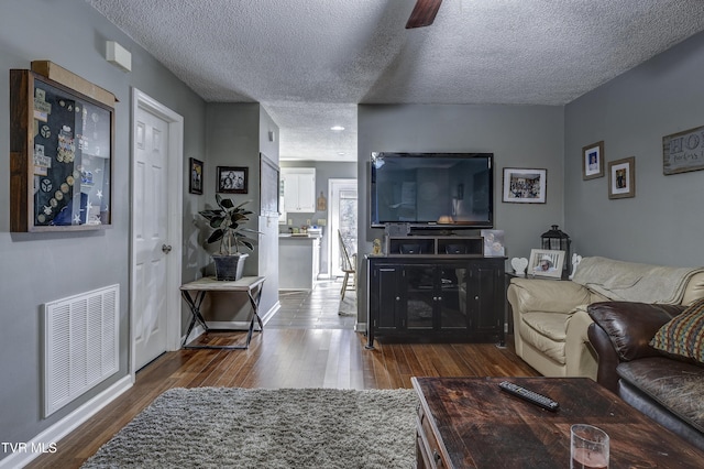 living room featuring ceiling fan, dark hardwood / wood-style flooring, and a textured ceiling