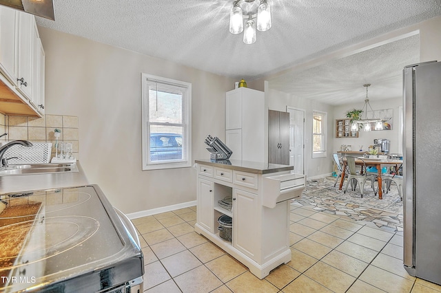 kitchen with sink, appliances with stainless steel finishes, white cabinetry, hanging light fixtures, and light tile patterned flooring