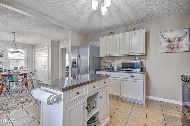 kitchen with light tile patterned flooring, appliances with stainless steel finishes, tasteful backsplash, white cabinetry, and hanging light fixtures