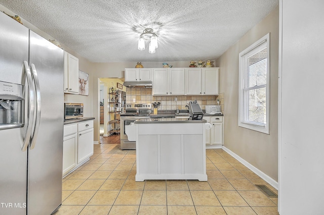 kitchen with stainless steel appliances, white cabinetry, light tile patterned floors, and decorative backsplash