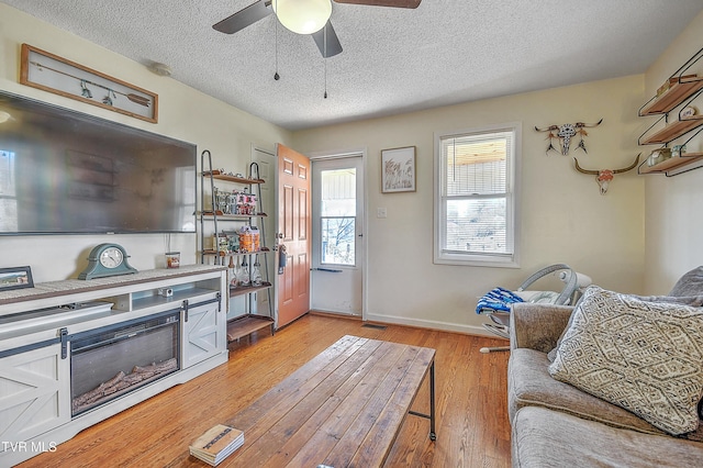 living room featuring ceiling fan, light hardwood / wood-style flooring, and a textured ceiling