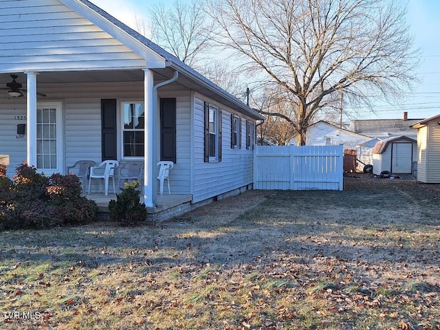 view of side of property featuring ceiling fan, a lawn, and a storage shed