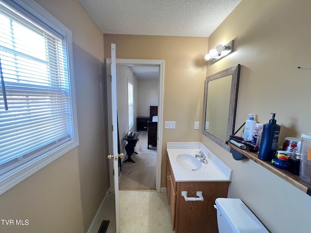 bathroom with a textured ceiling, toilet, vanity, and a healthy amount of sunlight