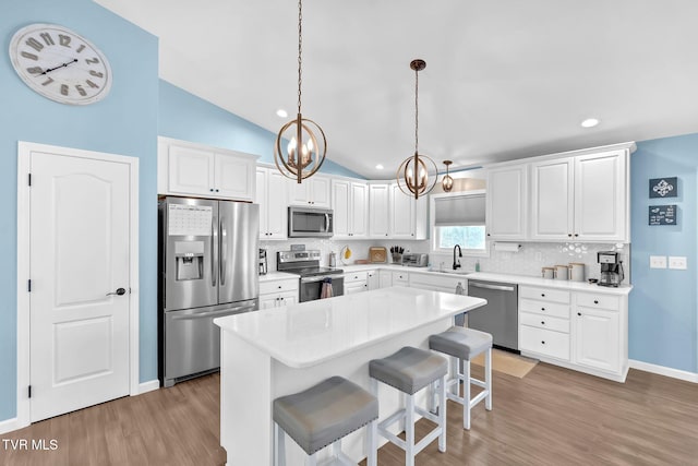 kitchen featuring lofted ceiling, white cabinetry, a kitchen breakfast bar, pendant lighting, and stainless steel appliances