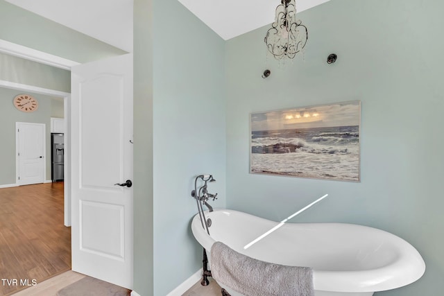 bathroom with wood-type flooring, an inviting chandelier, and a tub to relax in