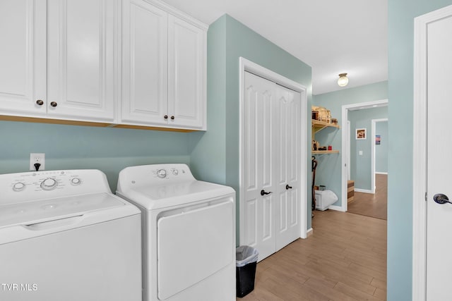 clothes washing area featuring cabinets, washing machine and clothes dryer, and light hardwood / wood-style flooring