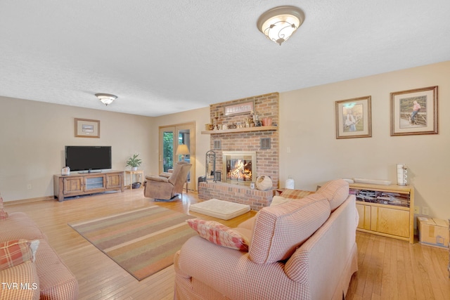 living room featuring a textured ceiling, a brick fireplace, and light wood-type flooring