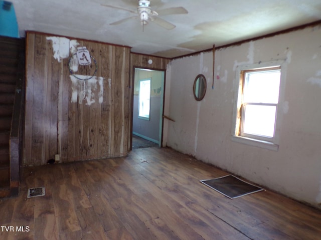 spare room featuring dark wood-type flooring, wooden walls, and ceiling fan