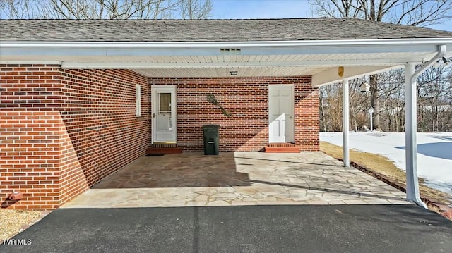 snow covered property entrance with a carport