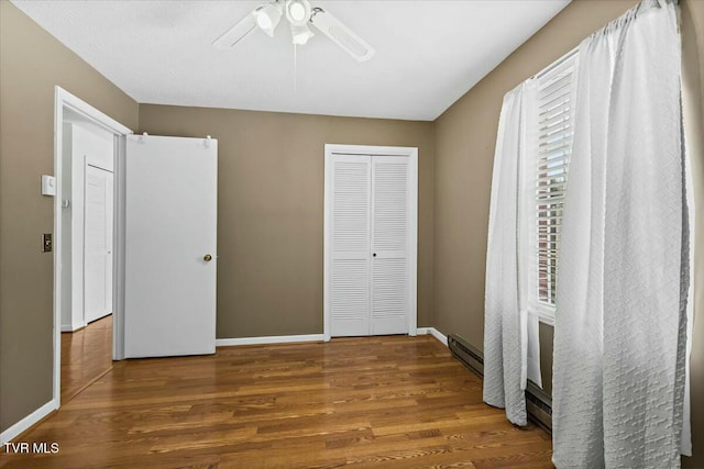 unfurnished bedroom with baseboard heating, ceiling fan, and wood-type flooring