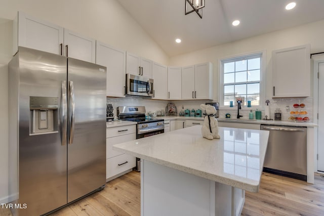 kitchen with appliances with stainless steel finishes, white cabinets, light stone countertops, a kitchen island, and lofted ceiling