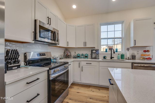 kitchen featuring white cabinets, stainless steel appliances, light stone countertops, and sink