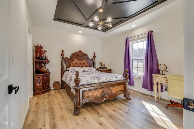 bedroom with a chandelier, light hardwood / wood-style flooring, and a tray ceiling