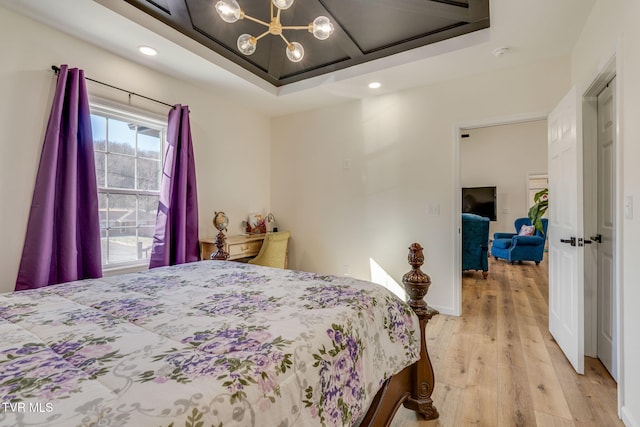 bedroom with light wood-type flooring, a chandelier, and a raised ceiling