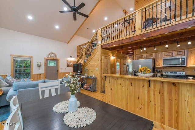 dining area with ceiling fan, high vaulted ceiling, track lighting, and wooden walls