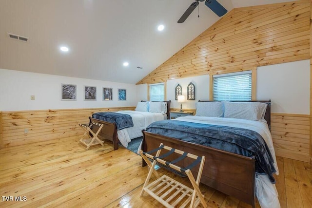 bedroom featuring wood-type flooring, wooden walls, high vaulted ceiling, and multiple windows