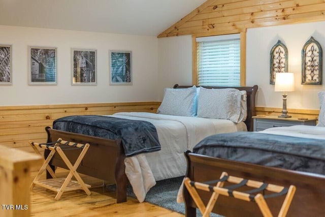 bedroom with lofted ceiling, wooden walls, and light hardwood / wood-style floors