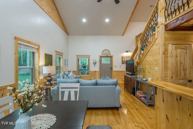 living room with high vaulted ceiling, wooden walls, light hardwood / wood-style floors, and ceiling fan