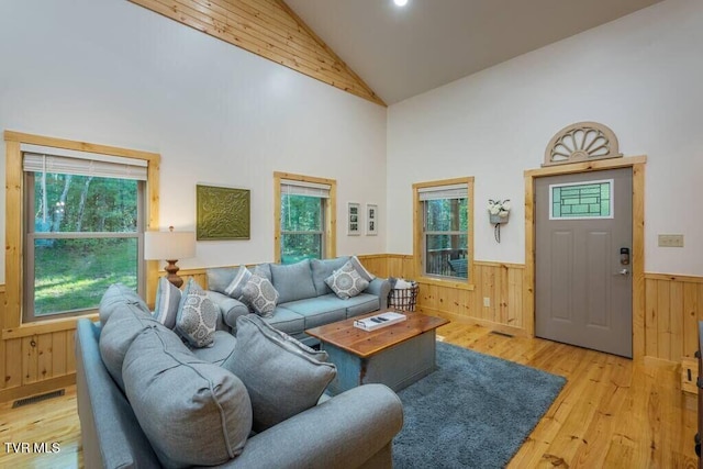 living room with high vaulted ceiling, plenty of natural light, light hardwood / wood-style floors, and wood walls