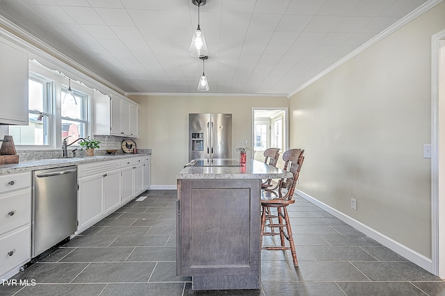 kitchen with a center island, appliances with stainless steel finishes, white cabinetry, sink, and decorative light fixtures