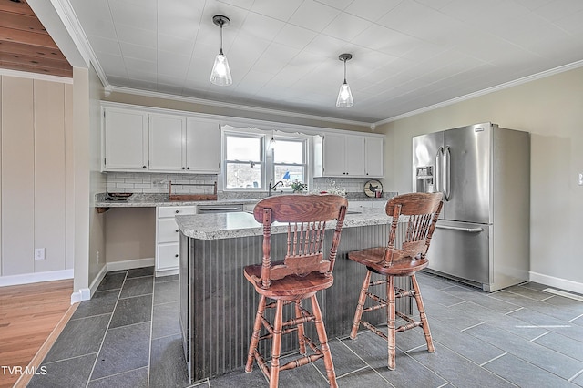 kitchen featuring pendant lighting, stainless steel fridge, white cabinetry, ornamental molding, and a kitchen island