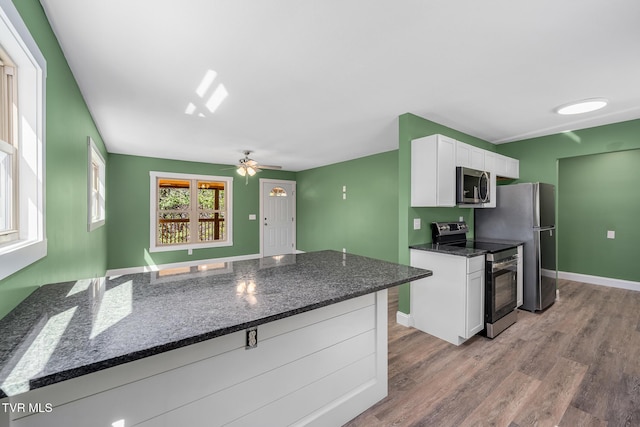 kitchen with light wood-style flooring, appliances with stainless steel finishes, white cabinets, dark stone counters, and a peninsula