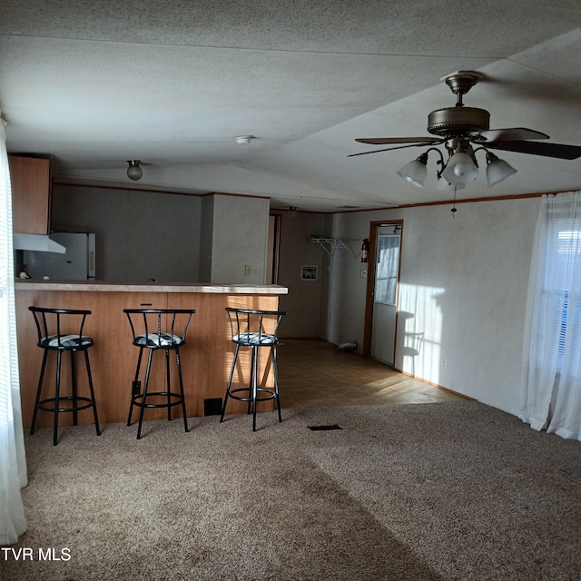 kitchen featuring stainless steel refrigerator, carpet flooring, a kitchen bar, ceiling fan, and kitchen peninsula