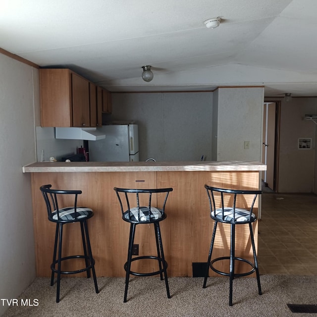 kitchen featuring lofted ceiling, fridge, a breakfast bar, and kitchen peninsula