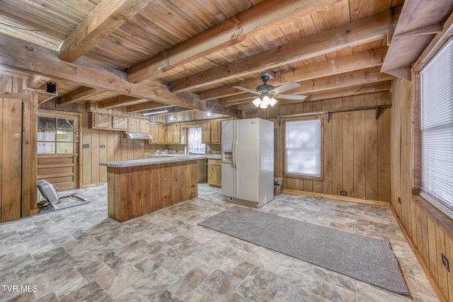 kitchen featuring white refrigerator with ice dispenser, wooden walls, and a healthy amount of sunlight