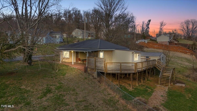 back of property at dusk with a yard, stairs, metal roof, and a wooden deck