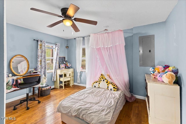 bedroom with ceiling fan, electric panel, baseboards, and wood finished floors