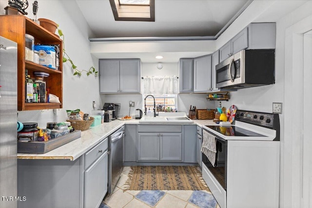 kitchen with stainless steel appliances, gray cabinets, a sink, and open shelves