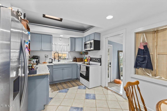 kitchen featuring a raised ceiling, appliances with stainless steel finishes, light countertops, gray cabinetry, and a sink