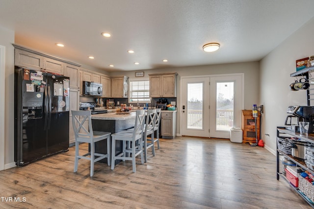 kitchen featuring a kitchen island, black appliances, light hardwood / wood-style floors, a kitchen bar, and light brown cabinetry