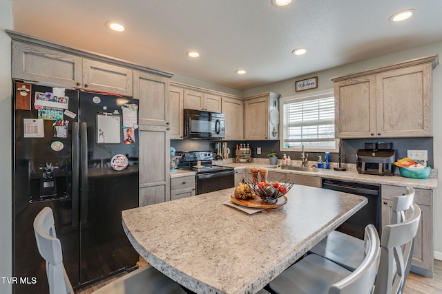 kitchen with a kitchen bar, sink, a kitchen island, light hardwood / wood-style floors, and black appliances