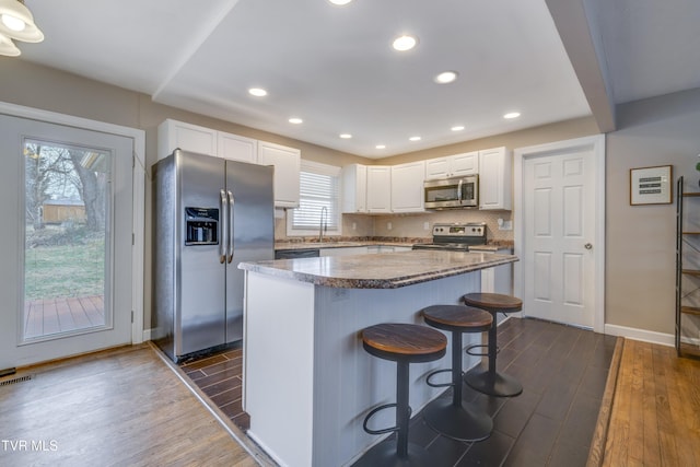 kitchen with a kitchen island, dark wood-type flooring, white cabinets, and appliances with stainless steel finishes