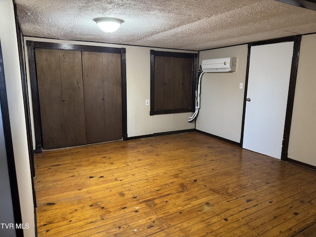 unfurnished bedroom featuring a wall unit AC, a textured ceiling, and light hardwood / wood-style floors