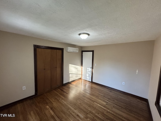 unfurnished bedroom featuring dark hardwood / wood-style flooring, a wall unit AC, a closet, and a textured ceiling