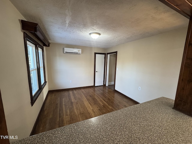 unfurnished room featuring dark wood-type flooring, a wall mounted AC, and a textured ceiling