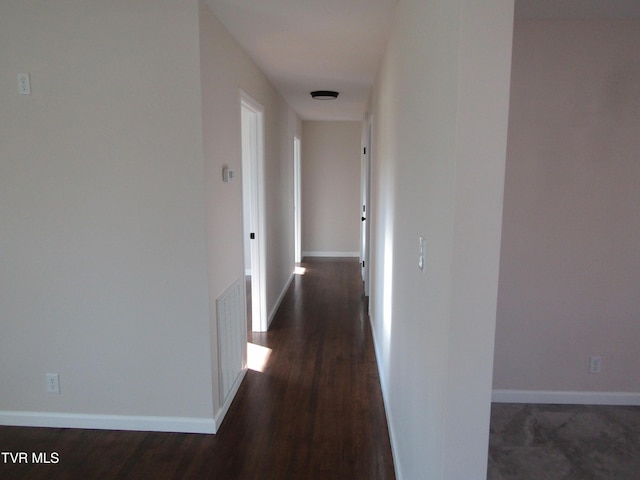 corridor featuring visible vents, baseboards, and dark wood finished floors