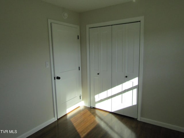 unfurnished bedroom featuring a closet, dark wood-style flooring, and baseboards