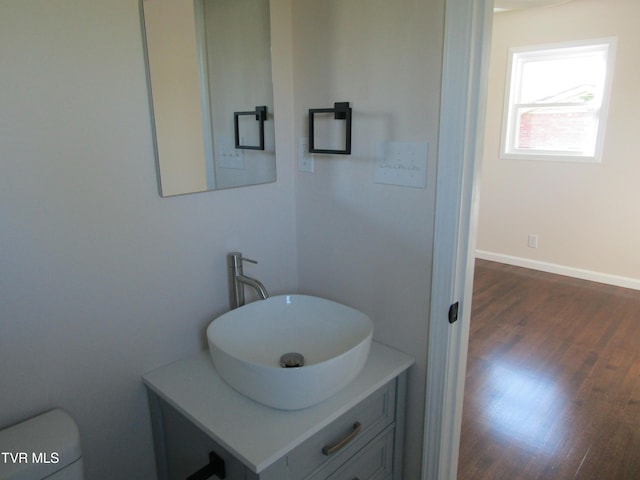 bathroom with toilet, wood finished floors, vanity, and baseboards
