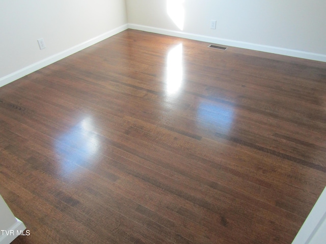 empty room featuring baseboards, dark wood-style floors, and visible vents