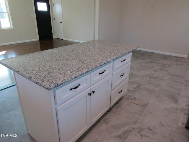 kitchen with white cabinets, a center island, light stone counters, and baseboards