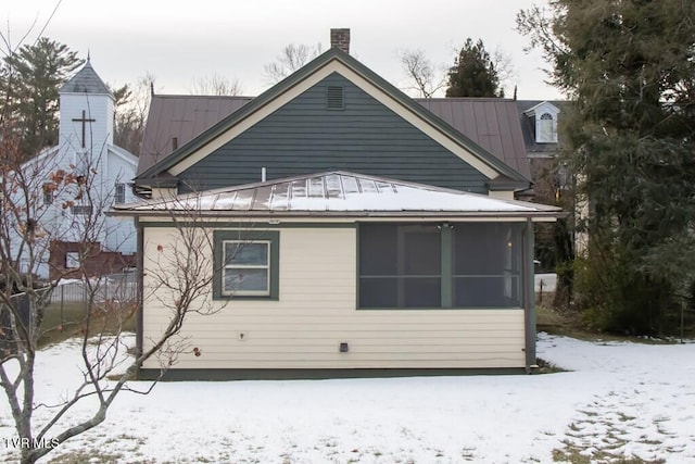 snow covered back of property with a sunroom