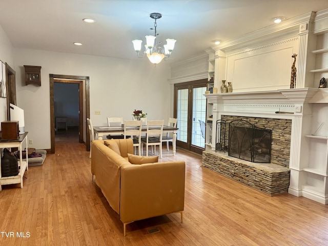 living room featuring built in features, a fireplace, crown molding, an inviting chandelier, and light hardwood / wood-style flooring